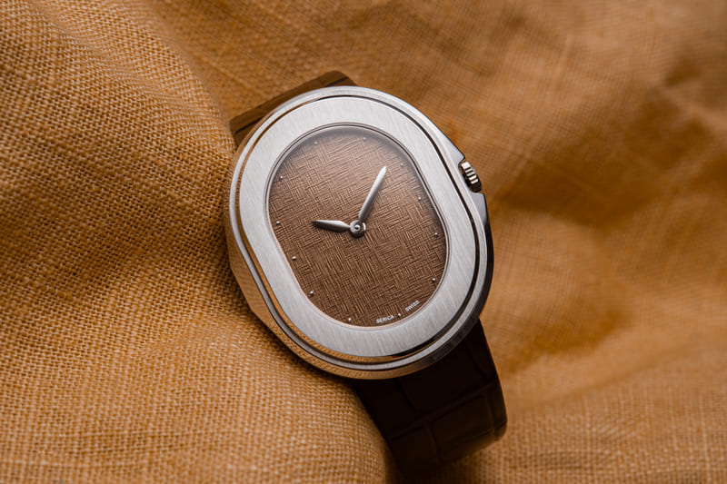 Luxury stainless steel Serica Parade 1174 dress watch with brown textured dial and leather strap, minimalist Swiss wristwatch close-up on fabric background